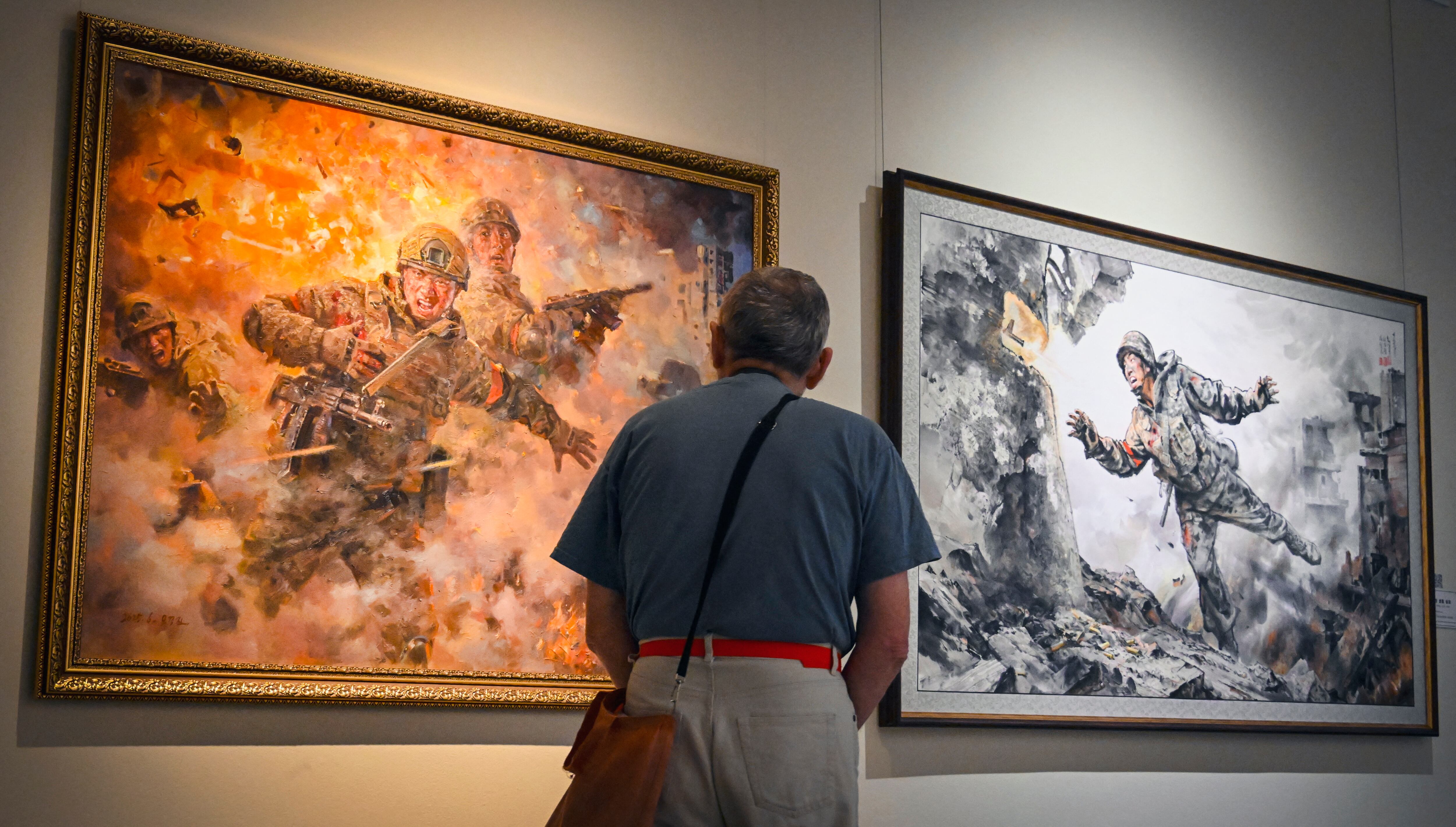 Un visitante pasa junto a las pinturas "Dando mi vida invaluable" de Chwe Il Bon, San Gum Chehor y Kim Cheol Yung (derecha) y "Para el camarada de combate" de Mueongjin Oh durante la exposición de arte norcoreano en Moscú el 2 de octubre de 2025. Alexander NEMENOV / AFP