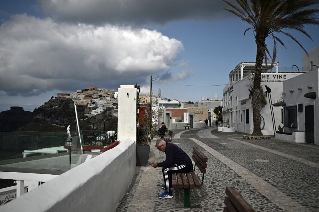 Un hombre mira su teléfono portátil mientras está sentado en un banco en una calle de Fira, en la isla griega de Santorini, el 3 de febrero de 2025 (Foto de Aris MESSINIS / AFP)