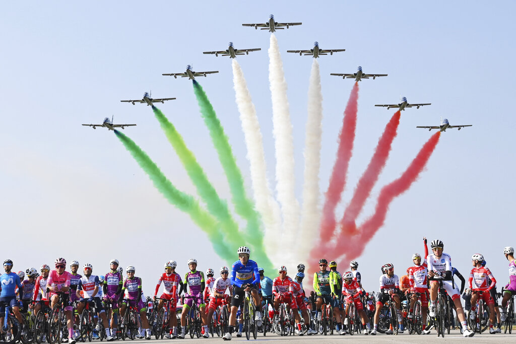 The pack of cyclists is backdropped by the Frecce Tricolori Italian Air Force aerobatic squad flying past, prior to the 15th stage of the Giro d'Italia cycling race, Italy, at the Rivolto air base, Sunday, Oct. 18, 2020. (Gian Mattia D'Alberto/LaPresse via AP)