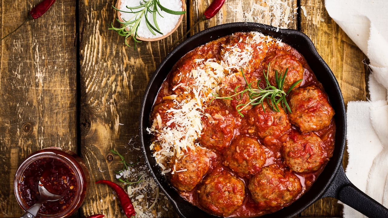 Albóndigas caseras en salsa de tomate agridulce con queso parmesano rallado encima sobre una mesa de madera rústica vista desde arriba