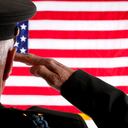 Senior adult veteran man in military dress uniform saluting the 50 star American flag.