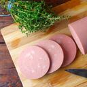 trozo de mortadela de cerdo cruda entera en una tabla de cortar con algunas rebanadas. comida italiana