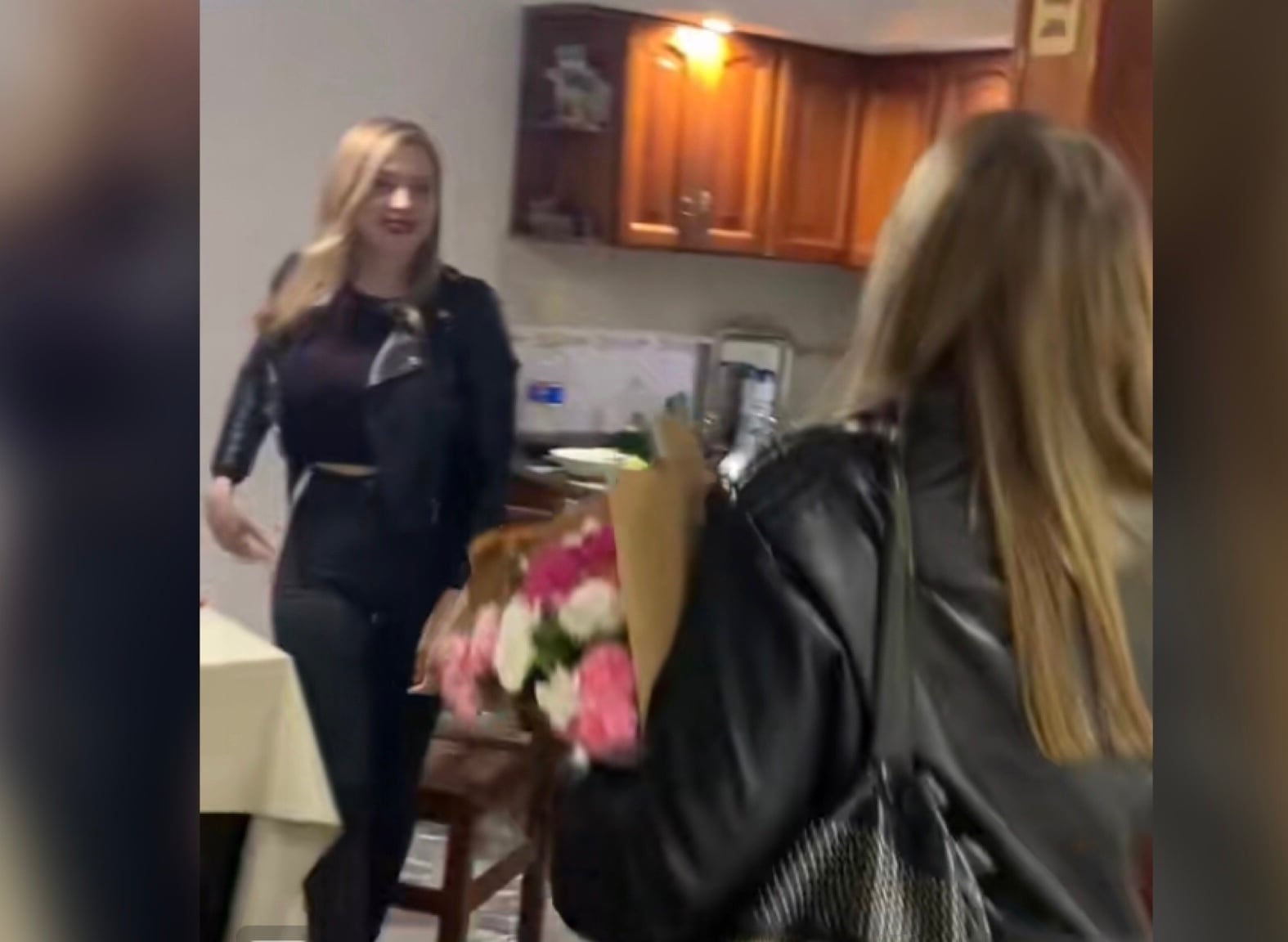 La madre y se dirige hacia la persona que se levanta del asiento para darle un beso en la mejilla.