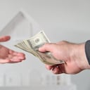 Two people (male and female) passing money against a white house. Mortgage, housing market, home loans and property, management concept. No people. Copy space