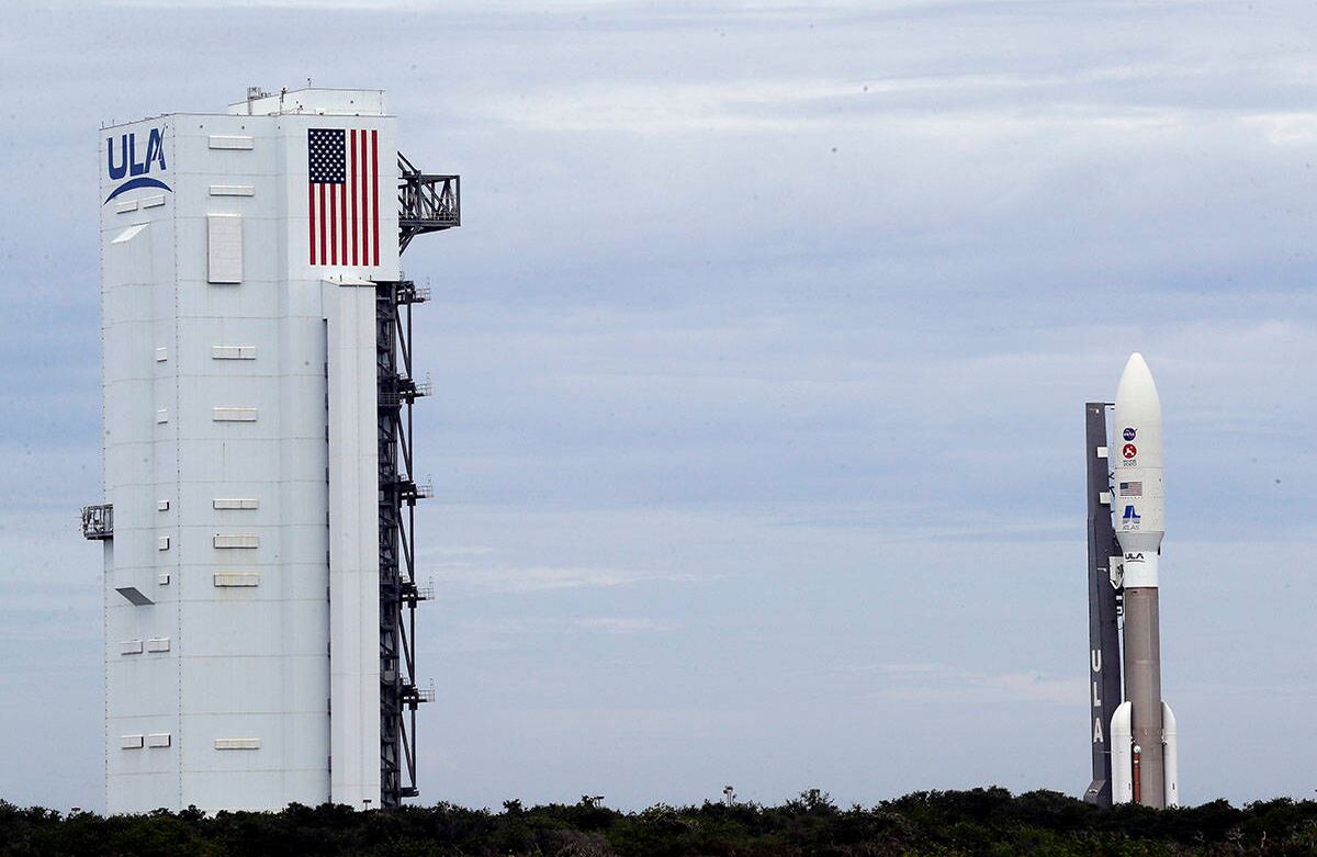 A la izquierda, un cohete United Launch Alliance Atlas V sale de la instalación de integración vertical, mientras se despliega al Complejo de Lanzamiento Espacial 41 en la Estación de la Fuerza Aérea de Cabo Cañaveral, el martes 28 de julio de 2020. El cohete programado para lanzarse el jueves aterrizará en Marte en febrero de 2021, el rover Mars 2020, llamado Perseverance, estudiará la geología marciana. Foto: John Raoux / AP  