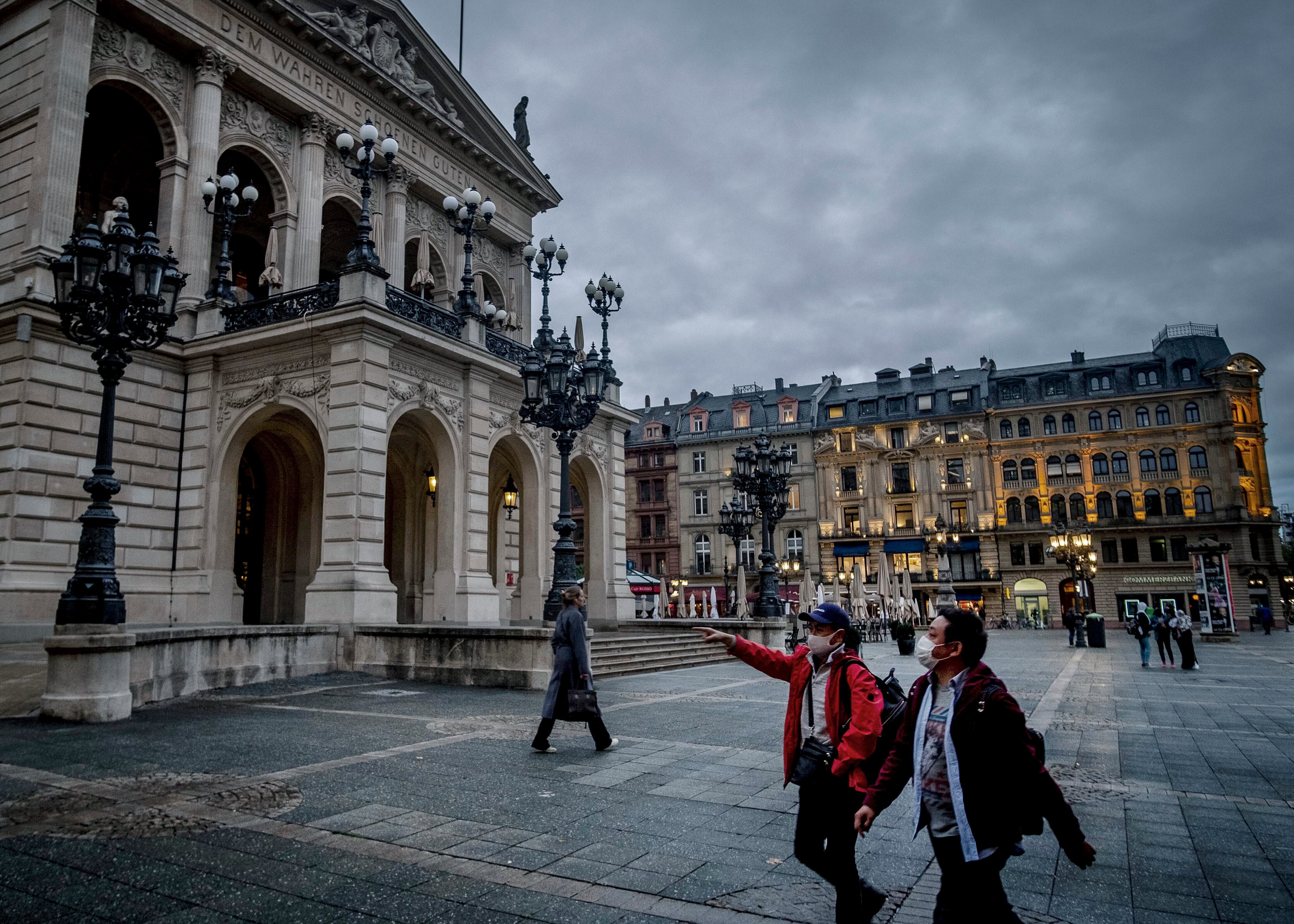 Dos personas con tapabocas caminan al frente de la Opera de Frankfurt, Alemania.