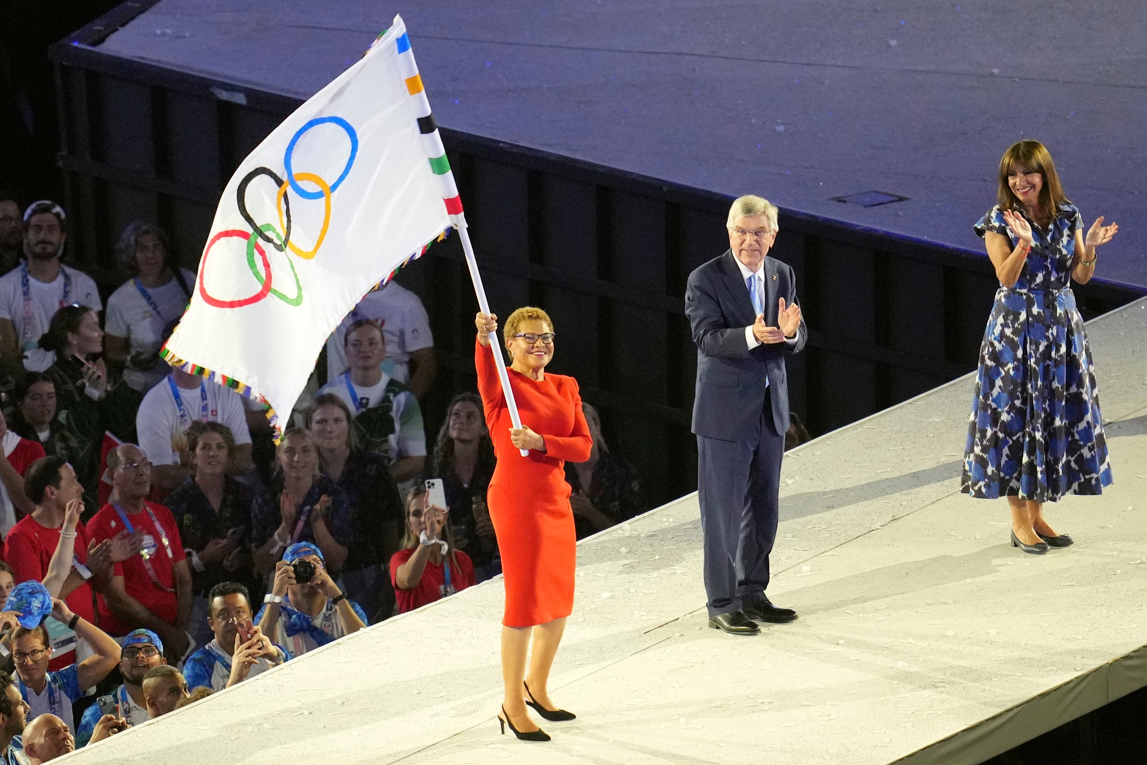 La alcaldesa de Los Ángeles, Karen Bass (izquierda), sostiene una bandera olímpica; el presidente del COI de San Francisco, Thomas Bach (centro), y la alcaldesa de París, Anne Hidalgo (derecha), miran durante la ceremonia de clausura de los Juegos Olímpicos de Verano de 2024 en el Stade de France, el domingo 11 de agosto de 2024, en Saint-Denis, Francia. (Foto AP/Kin Cheung)