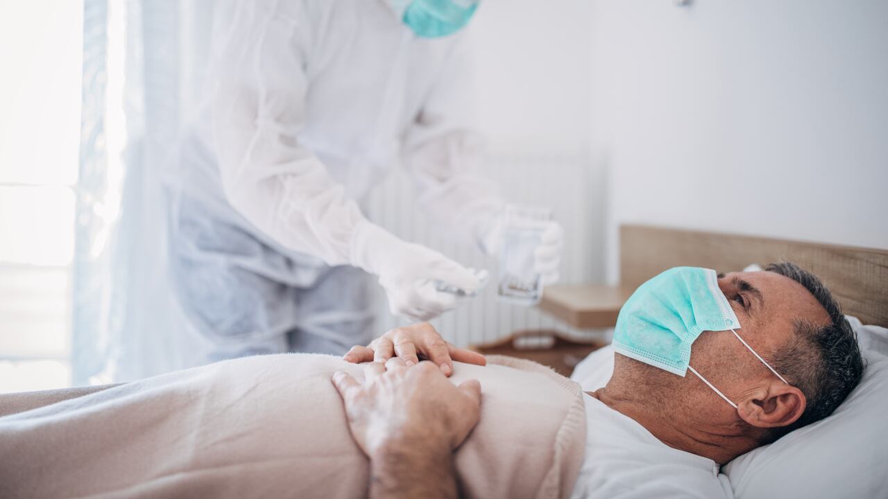 Man and woman, senior man lying in hospital bed because of coronavirus infection, female doctor is giving medicine to a patient.