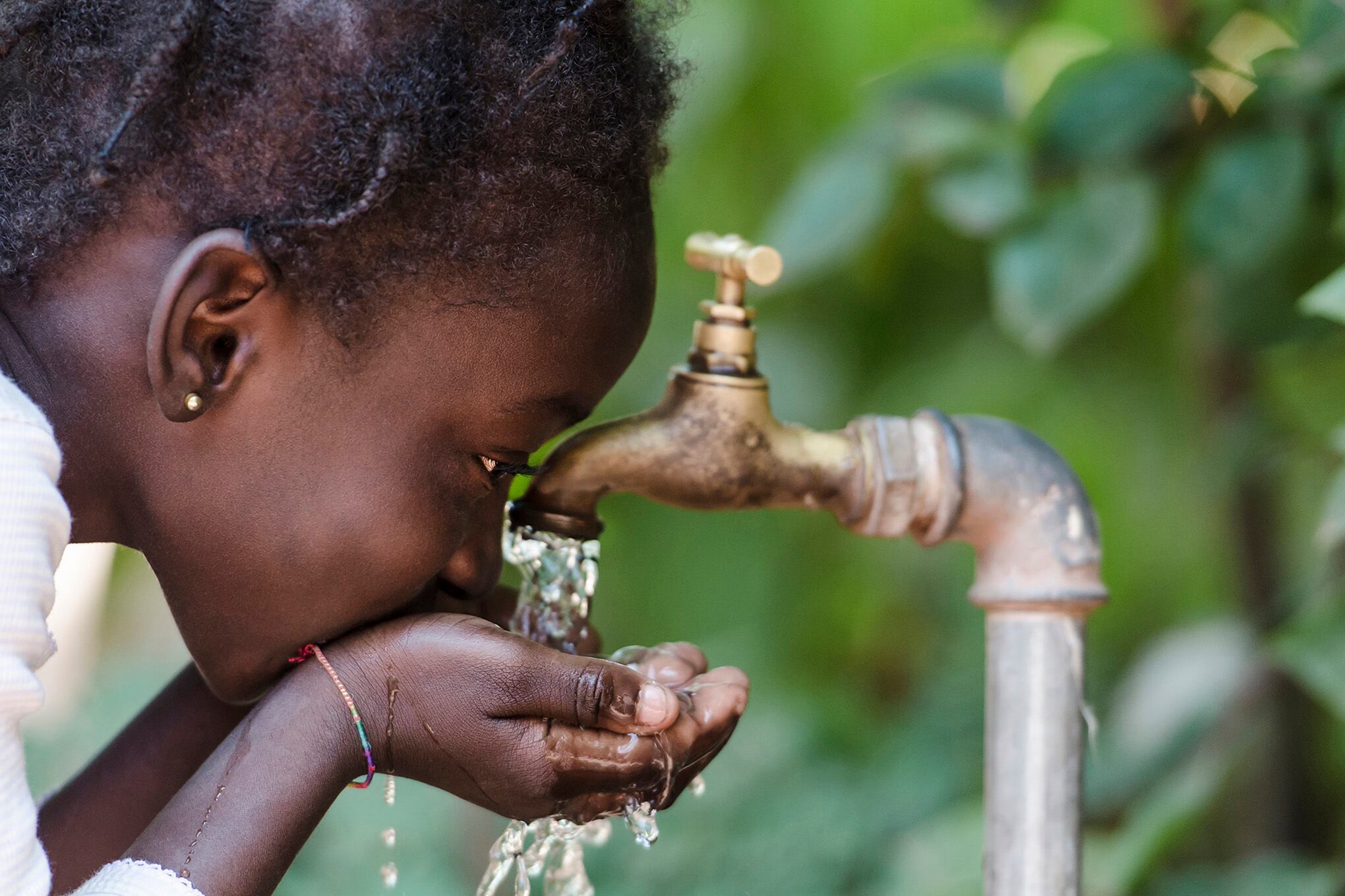 Niña negra bebiendo agua de grifo, niña tomando agua.