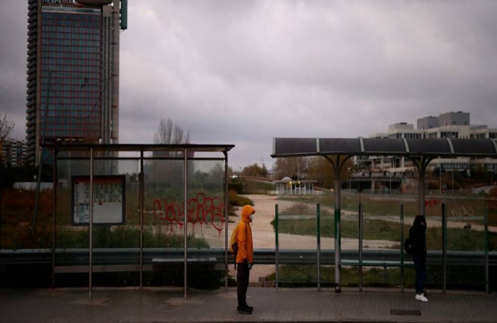 Dos personas con máscaras faciales esperan en una parada de autobús cerca del hospital Bellvitge, en inmediaciones a Barcelona. España se movió para extender un estado de emergencia hasta el 11 de abril para tratar de frenar la propagación del coronavirus después de que el país registrara 394 nuevas muertes por el enfermedad. Foto: Pau Barrena / AFP 