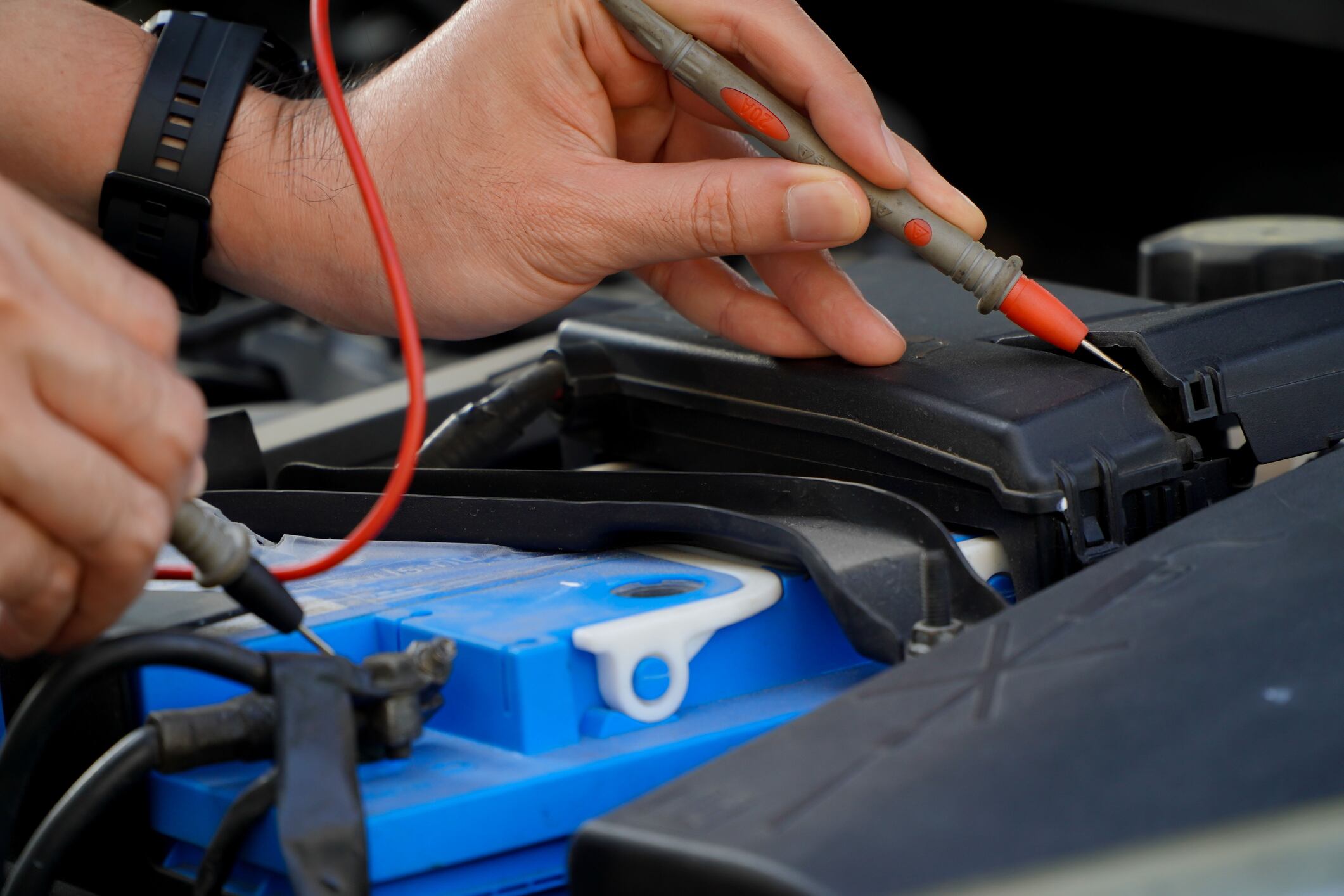 Un mecánico de automóviles utiliza un voltímetro multímetro para comprobar el nivel de voltaje en una batería de coche.