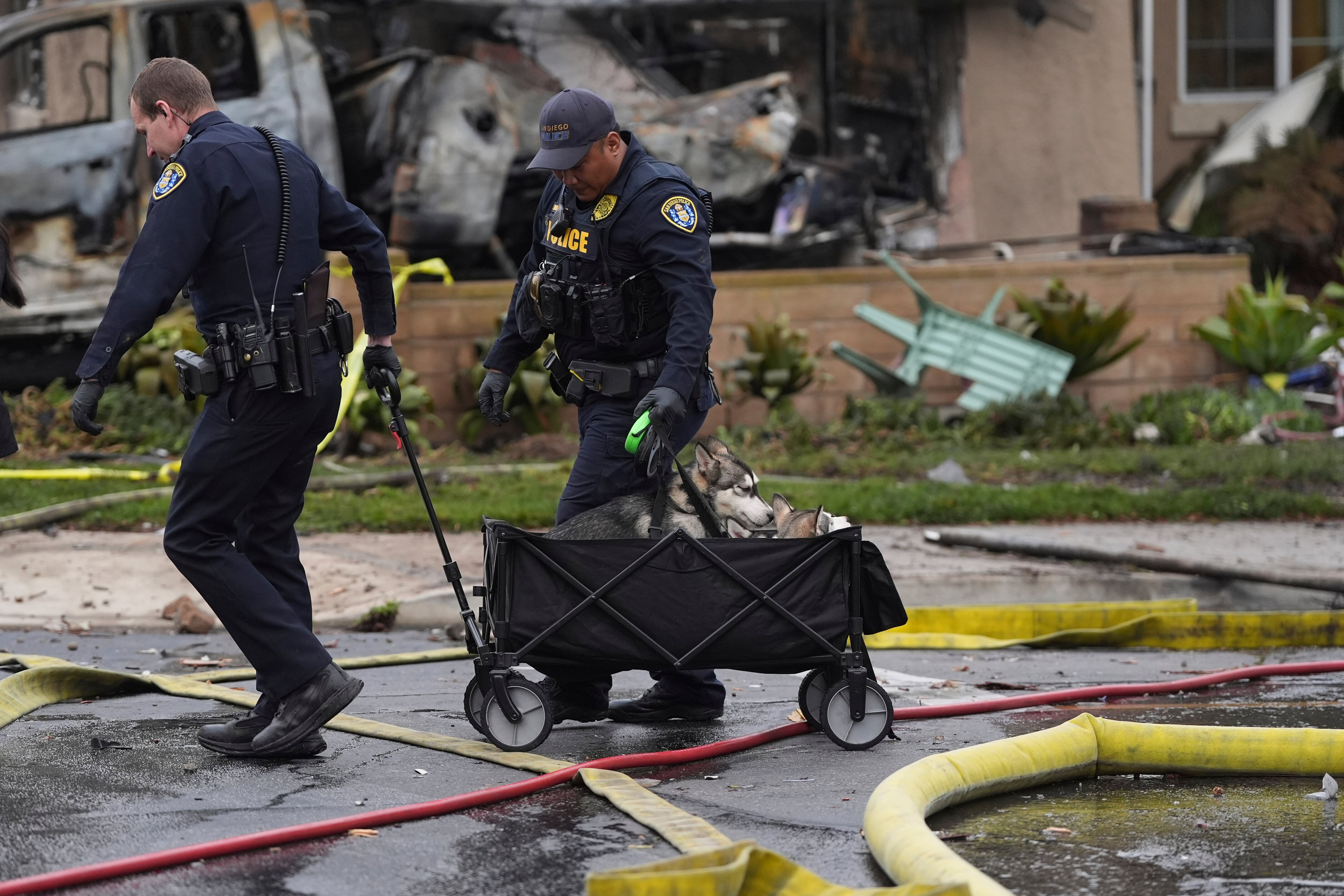 Police help rescue dogs from a home after a small plane crashed into a San Diego neighborhood earlier, setting several homes on fire and forcing evacuations along several blocks, Thursday, May 22, 2025. (AP Photo/Gregory Bull)