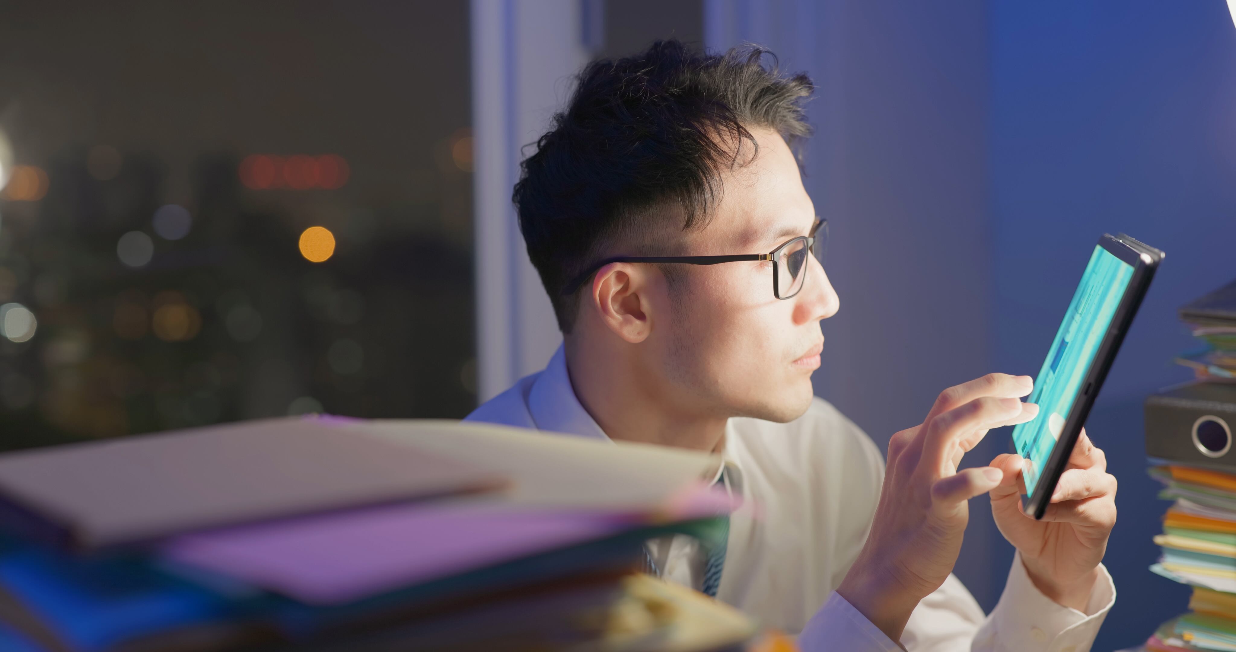 side view asian businessman wearing eyeglasses is overtime work and hardworking at night in office - he use digital tablet