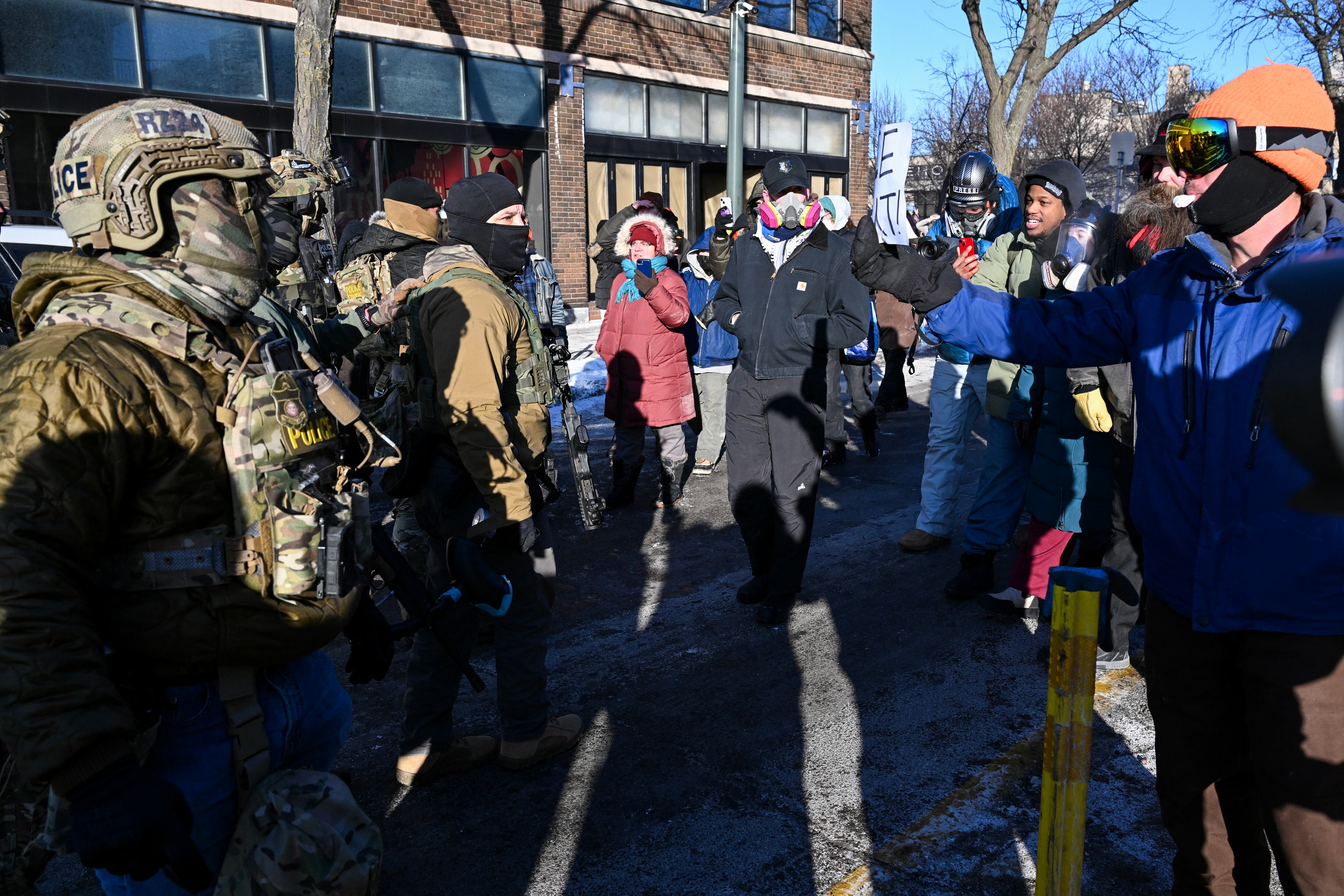 Federal agents (L) look on as demonstators gather near the site of where state and local authorities say a man was shot by federal agents earlier in the morning in Minneapolis, Minnesota, on January 24, 2026. Minnesota Governor Tim Walz said Saturday that federal agents deployed in Minneapolis as part of a sweeping immigration crackdown had carried out "another horrific shooting," less than three weeks after the fatal shooting of Renee Good. (Photo by ROBERTO SCHMIDT / AFP)