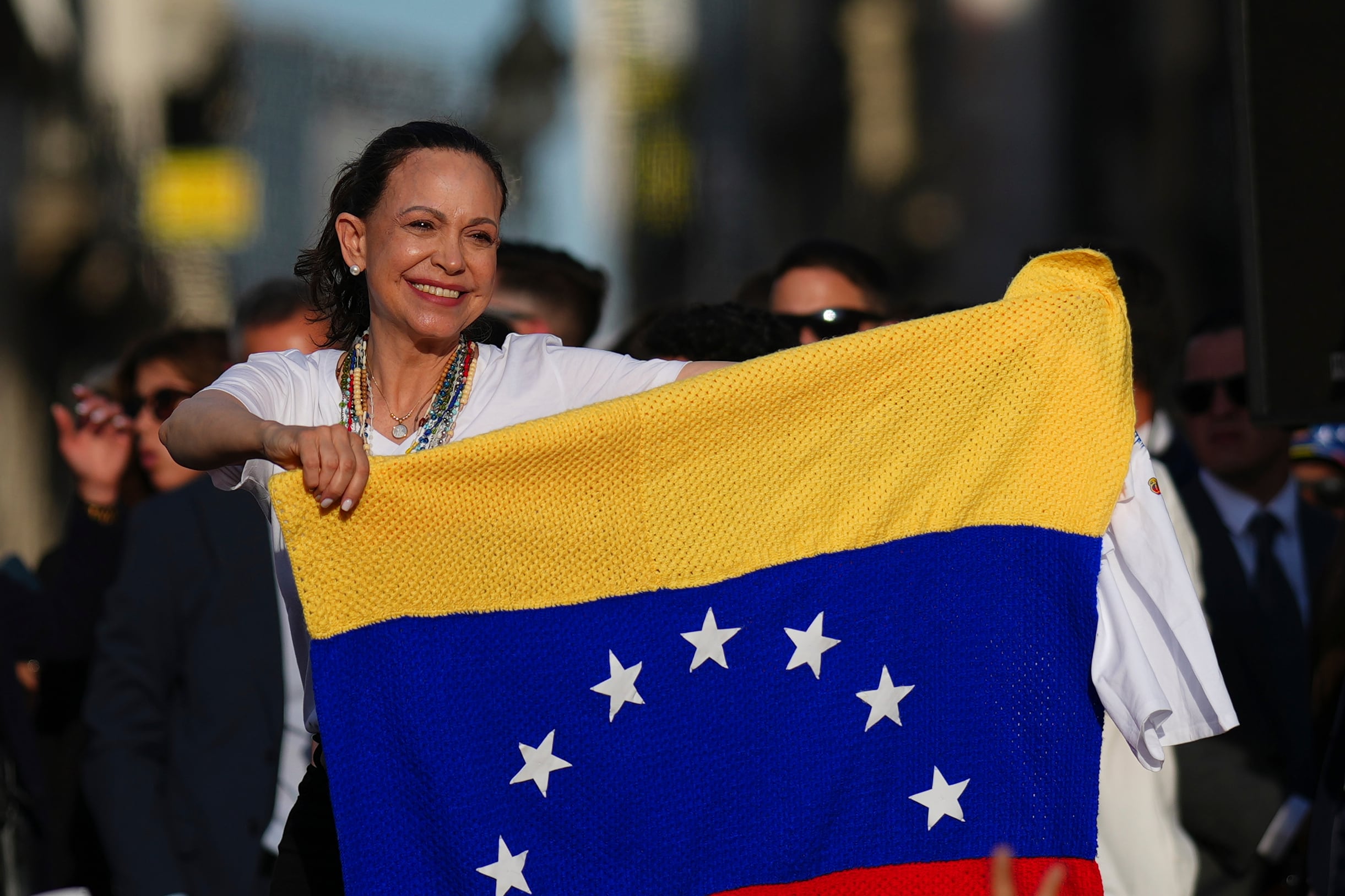 La líder de la oposición venezolana, María Corina Machado, sostiene una bandera venezolana en el escenario frente a sus seguidores en la Puerta del Sol de Madrid, España