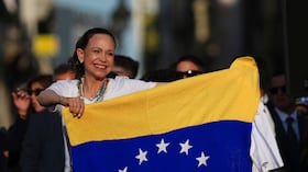 La líder de la oposición venezolana, María Corina Machado, sostiene una bandera venezolana en el escenario frente a sus seguidores en la Puerta del Sol de Madrid, España