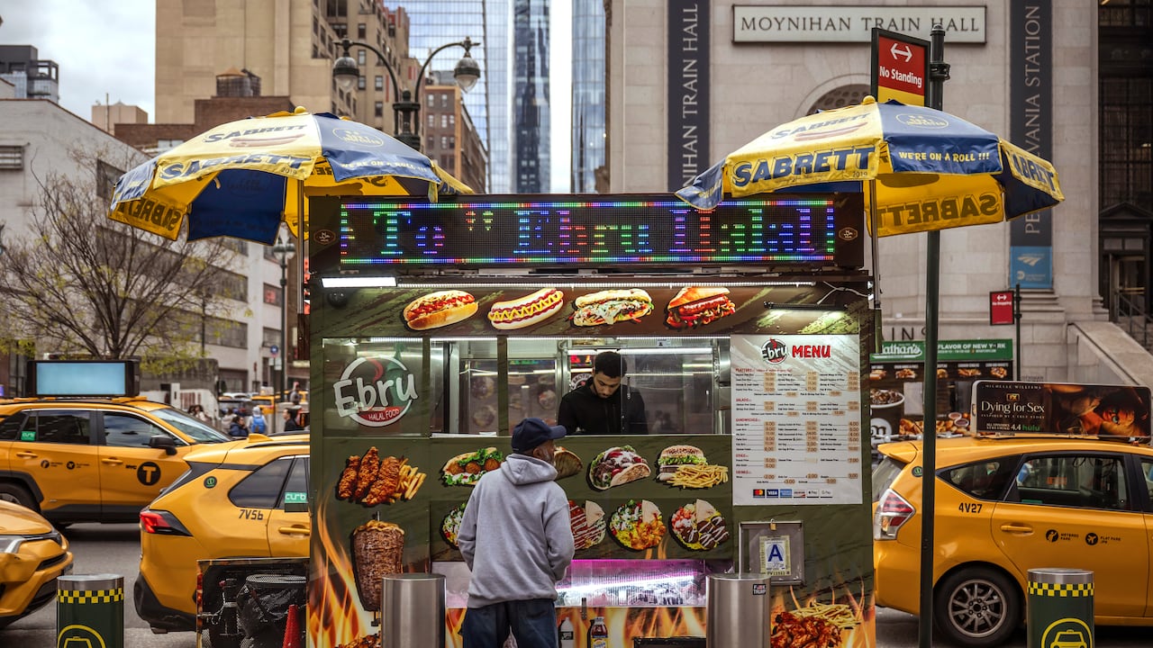 Un hombre compra comida a un vendedor ambulante frente a la terminal de trenes Moynihan en Midtown Manhattan el 13 de abril de 2025 en la ciudad de Nueva York.