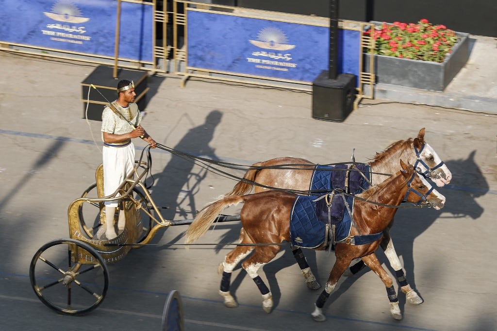 Un actor disfrazado monta un carro de dos caballos en la plaza Tahrir, en el centro de El Cairo. El 3 de abril de 2021 se realizó un un ensayo del desfile de 22 momias reales del antiguo Egipto que partirá del Museo Egipcio de Tahrir hacia su nuevo lugar de descanso en el nuevo Museo Nacional de la Civilización Egipcia (NMEC), a unos siete kilómetros al sur, en el histórico Fustat (El Cairo antiguo). - Bautizado como el Desfile Dorado de los Faraones, los 18 reyes y las cuatro reinas viajarán en orden, los más antiguos primero, cada uno a bordo de una carroza independiente decorada al estilo del antiguo Egipto. Foto de Khaled DESOUKI / AFP.