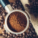 Espresso recién molido en un portafiltro, listo para convertirse en un espresso caliente. Fondo de madera rústica, una bolsa de café de arpillera en el fondo cubierta con granos de café tostados. Vista aérea.