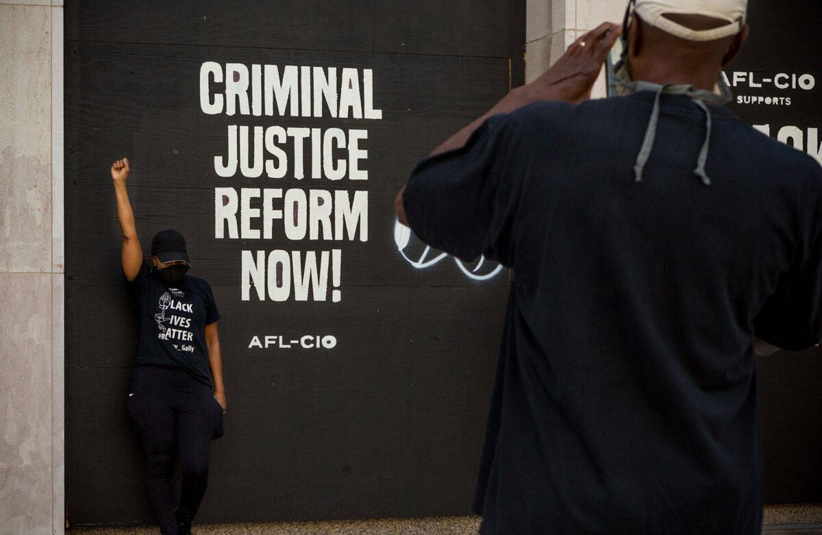 Manifestante posa delante de un mensaje exigiendo la Reforma de Sistema de Justicia Criminal. Las paredes y ventanas alrededor de Black Lives Matter Plaza y calles circundantes han sido tapiadas por protección a posibles destrozos y vandalismo. Muchas de ellas han sido cubiertas de mensajes de apoyo al movimiento BLM. Imagen tomada el 06 de junio de 2020  Washington DC- María Luz Bravo