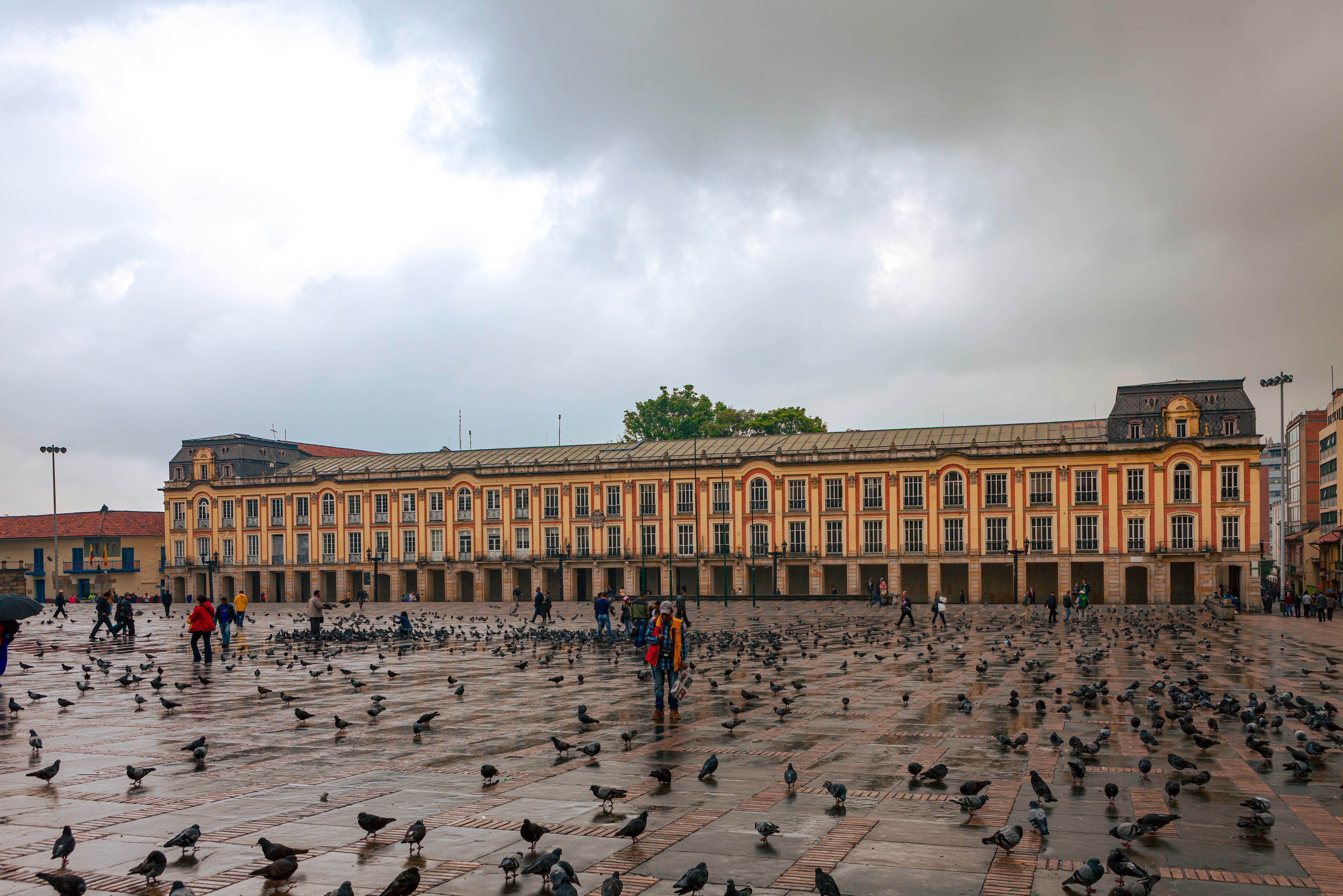 Bogotá, Colombia - 04 de abril de 2016: Mirando a través de la Plaza de Bolívar, la plaza más importante de la capital andina de Bogotá en Colombia, América del Sur. Es la segunda plaza más grande del país. Al otro lado de la Plaza está el Edificio Liévano que es la oficina del Alcalde de Bogotá. Diseñado por el arquitecto francés Lelarge, se completó en 1905. Ha estado lloviendo y las nubes oscuras en el cielo traerán más lluvia en breve. No hay mucha gente en la plaza debido a la lluvia. A las miles de palomas de la plaza no les importa la lluvia. La altitud al nivel de la calle es de unos 8.500 pies sobre el nivel medio del mar. Foto tomada en la luz del sol de la tarde. Formato horizontal. Copie el espacio.