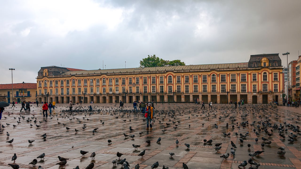 Bogotá, Colombia - 04 de abril de 2016: Mirando a través de la Plaza de Bolívar, la plaza más importante de la capital andina de Bogotá en Colombia, América del Sur. Es la segunda plaza más grande del país. Al otro lado de la Plaza está el Edificio Liévano que es la oficina del Alcalde de Bogotá. Diseñado por el arquitecto francés Lelarge, se completó en 1905. Ha estado lloviendo y las nubes oscuras en el cielo traerán más lluvia en breve. No hay mucha gente en la plaza debido a la lluvia. A las miles de palomas de la plaza no les importa la lluvia. La altitud al nivel de la calle es de unos 8.500 pies sobre el nivel medio del mar. Foto tomada en la luz del sol de la tarde. Formato horizontal. Copie el espacio.