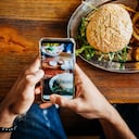 Un hombre tomando una foto de su hamburguesa artesanal con su teléfono inteligente antes de comerla.