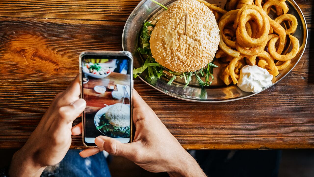 Un hombre tomando una foto de su hamburguesa artesanal con su teléfono inteligente antes de comerla.