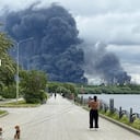 Varias personas pasean por un parque mientras una densa columna de humo negro se eleva desde la refinería de petróleo de Gazprom Neft, la petrolera rusa ubicada en las afueras del sureste de Moscú, el 18 de junio de 2026.