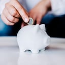 Putting a coin in a white piggy bank at home.