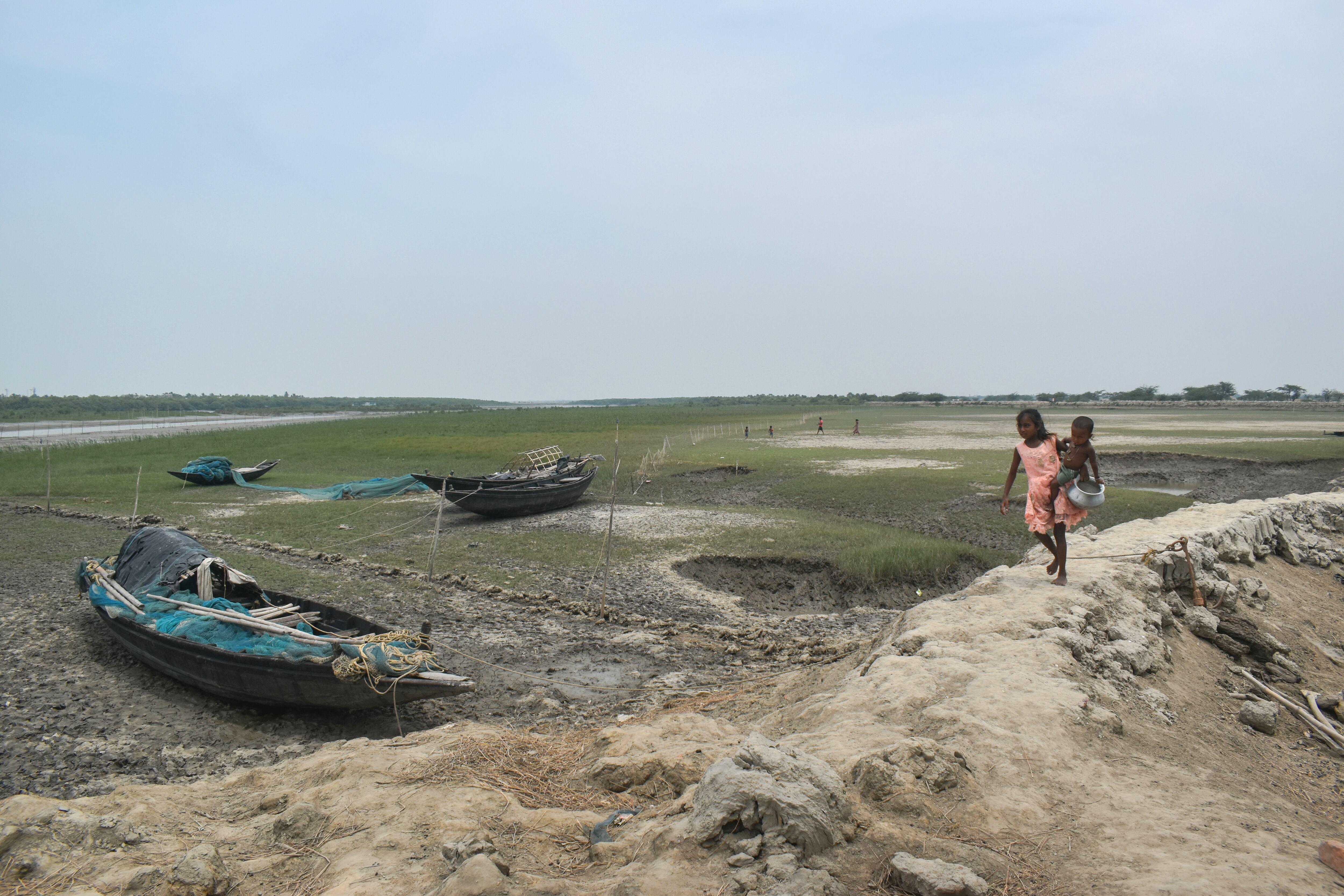 Una niña carga a un niño y pasa junto al lecho de un río casi seco en un caluroso día de verano para recolectar agua potable en las afueras de Calcuta, India