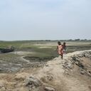 Una niña carga a un niño y pasa junto al lecho de un río casi seco en un caluroso día de verano para recolectar agua potable en las afueras de Calcuta, India