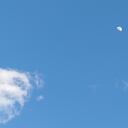 A bright blue sky contrasted by puffy white clouds and the bright moon.