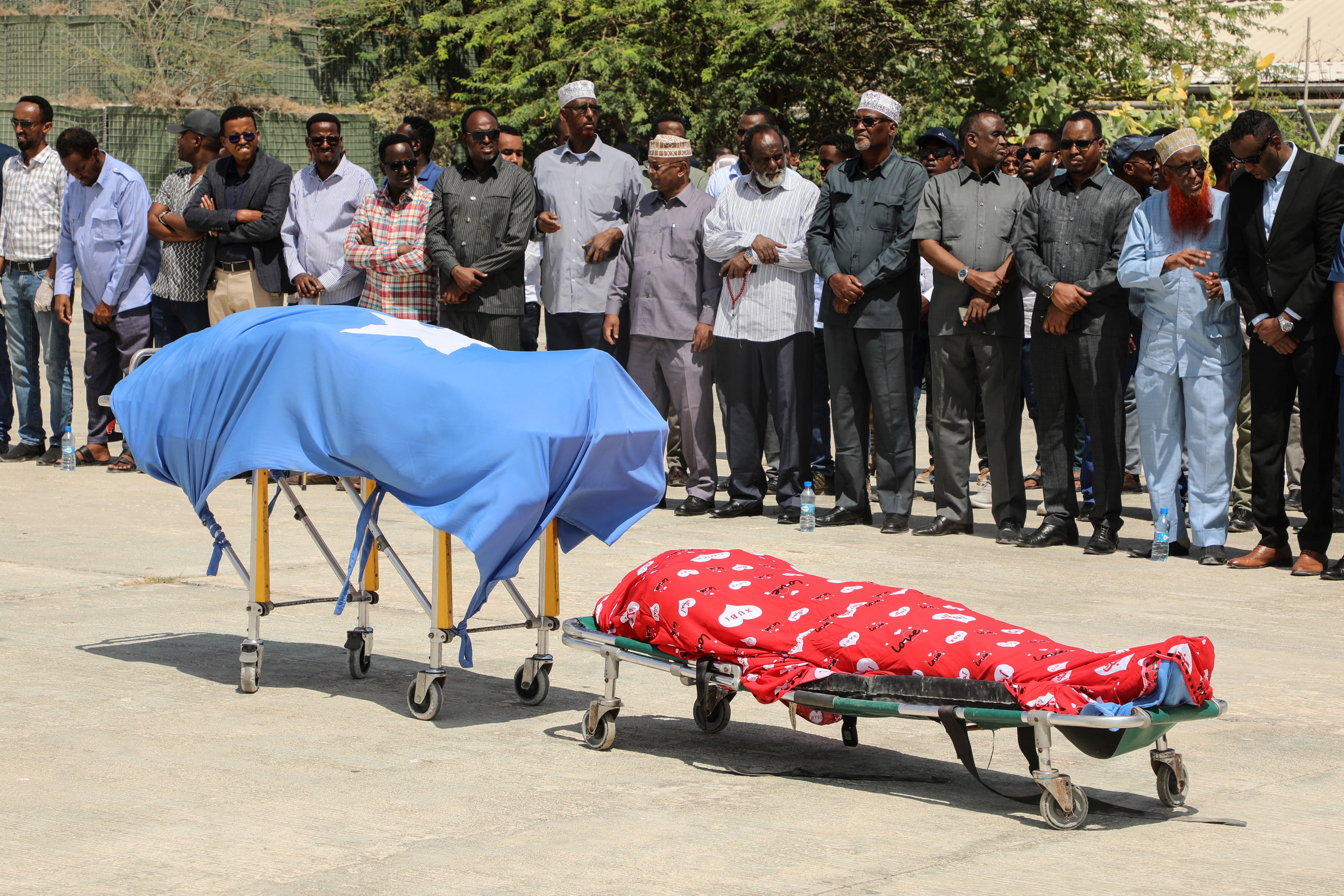 Los líderes políticos oran frente a los dos cuerpos de los legisladores locales, incluida Amina Mohamed Abdi, después de ser trasladados en avión desde Beledweyne, en el Aeropuerto Internacional Aden Adde en Mogadiscio, Somalia, el 24 de marzo de 2022. - El número de muertos por ataques gemelos en el centro de Somalia el 24 de marzo de 2022. La noche del 23 de marzo de 2022 superó los 30, dijo a la AFP el jefe de policía del distrito de Beledweyne el 24 de marzo de 2022, y el grupo insurgente Al-Shabaab dijo que estaba atacando a los políticos antes de las elecciones. (Foto de Hassan Ali ELMI / AFP)