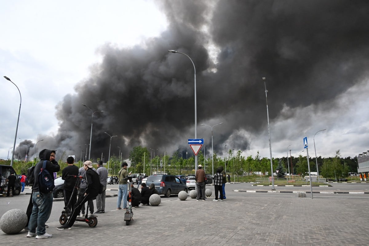 Se observa a varias personas frente a un centro comercial mientras una densa columna de humo negro se eleva desde la refinería de petróleo de Gazprom Neft, la petrolera rusa ubicada en las afueras del sureste de Moscú.