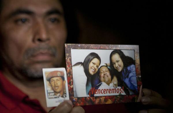 Un hombre porta el último retrato de Chávez junto a sus hijas. 