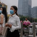 Varias personas con mascarillas para protegerse del coronavirus observan algo junto a un vendedor de flores afuera de una estación del tren subterráneo en Beijing. (AP Foto/Andy Wong)