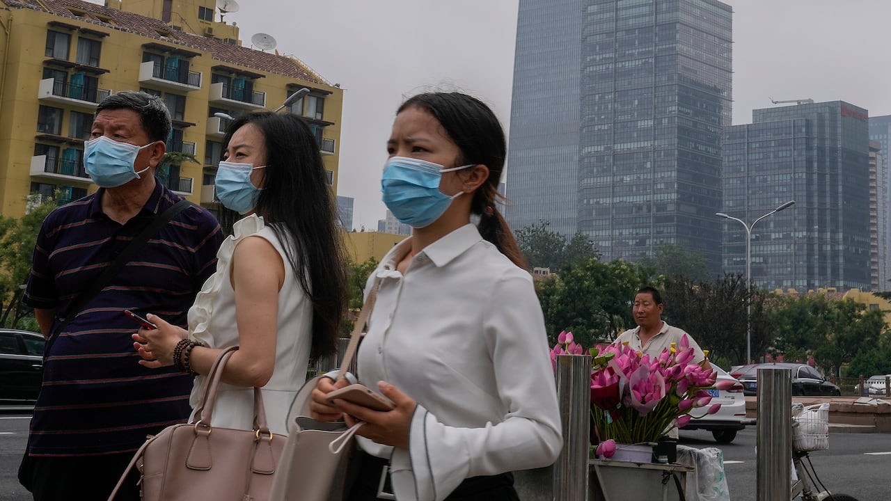 Varias personas con mascarillas para protegerse del coronavirus observan algo junto a un vendedor de flores afuera de una estación del tren subterráneo en Beijing. (AP Foto/Andy Wong)