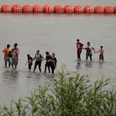 Migrantes que cruzaron el río Grande (Bravo) desde México caminan frente a enormes boyas colocadas como una barrera fronteriza flotante en el río, el miércoles 12 de julio de 2023, en Eagles Pass, Texas. (AP Foto/Eric Gay)