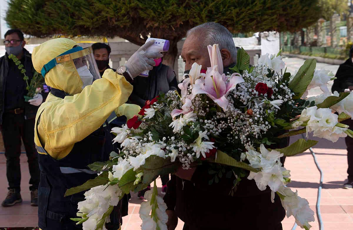 Un trabajador de la ciudad que usa equipo de protección completo como precaución contra la propagación del nuevo coronavirus, mide la temperatura de un pariente que llega para asistir a un servicio de entierro en el Cementerio General, en La Paz, Bolivia, el martes 21 de julio de 2020. La persona la muerte no estaba relacionada con covid-19. (Foto AP / Juan Karita)