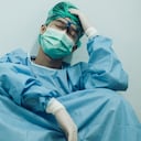 Médico con dolor de cabeza y cansado del trabajo mientras usa traje de PPE para proteger la enfermedad del coronavirus. El bienestar y la resiliencia emocional son componentes clave para mantener los servicios de atención esenciales.