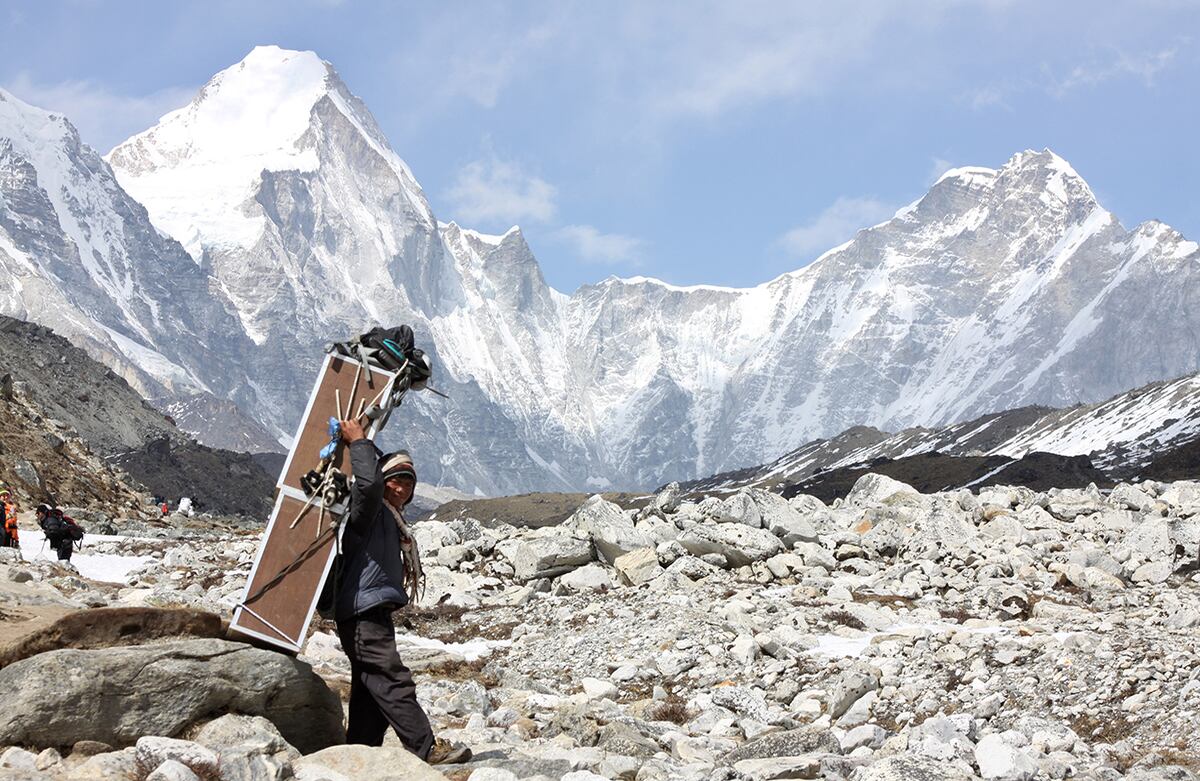 Un hombre carga cajas que contienen tanques de oxígeno para dirigirse hacia el Campamento Everest, al fondo aparece la montaña Lingtren (izq.) y la montaña Khumbutse (der.), en Nepal. (AP)