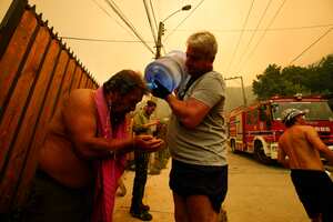 A man helps a fellow resident cool down with bottled water as forest fires burn nearby, in Vina del Mar, Chile, Saturday, Feb. 3, 2024. Officials say intense forest fires burning around a densely populated area of central Chile have left several people dead and destroyed hundreds of homes. (AP Photo/Esteban Felix)