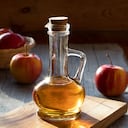 A bottle of apple cider vinegar in the morning sun, with apples in the background