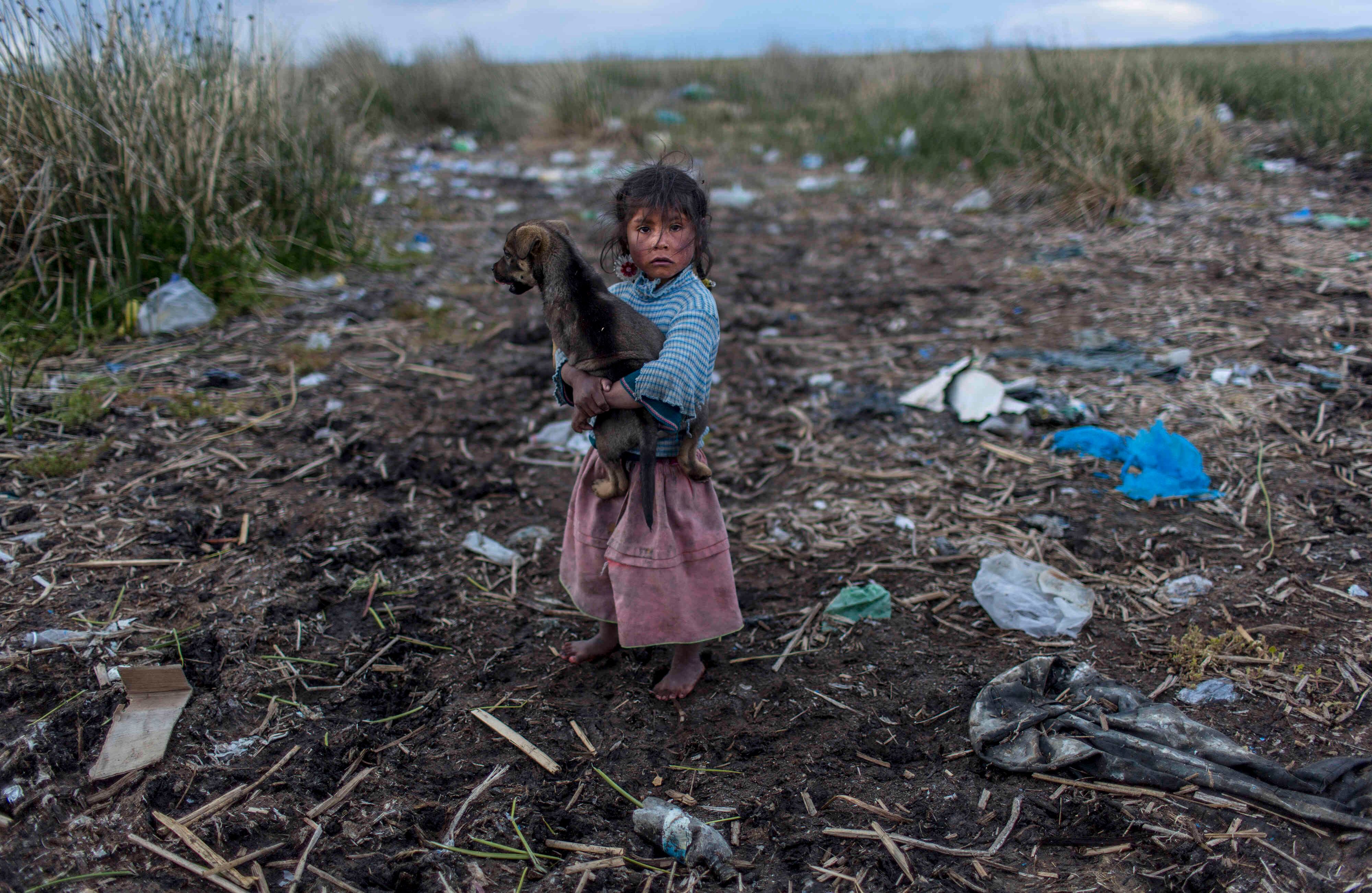 En esta foto del 4 de febrero de 2017, Melinda Quispe camina sobre la basura del lago Titicaca, donde ella sostiene su perro, en su pueblo Kapi Cruz Grande, en la región de Puno, Perú. Los gobiernos de Perú y Bolivia firmaron un pacto en enero para gastar más de 500 millones de dólares para atacar el problema de contaminación del lago Titicaca (AP Photo / Rodrigo Abd) 