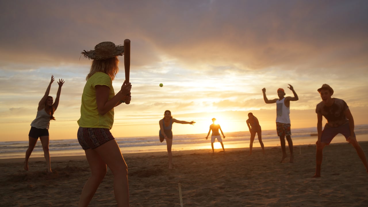Grupo de jóvenes jugando béisbol en la playa, al atardecer