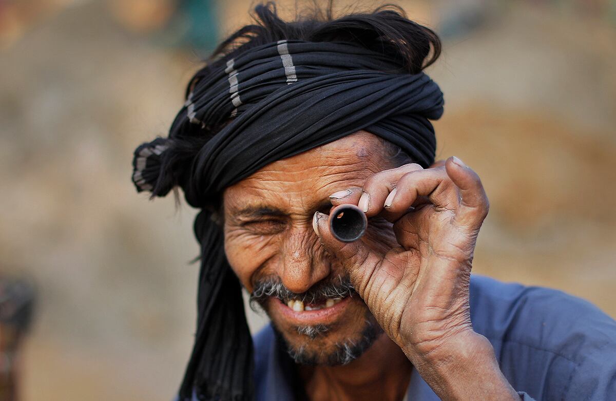 Un hombre de la India mira a través de una pipa de arcilla usada para fumar tabaco, cerca a un barrio pobre en Delhi, India. (AP)
