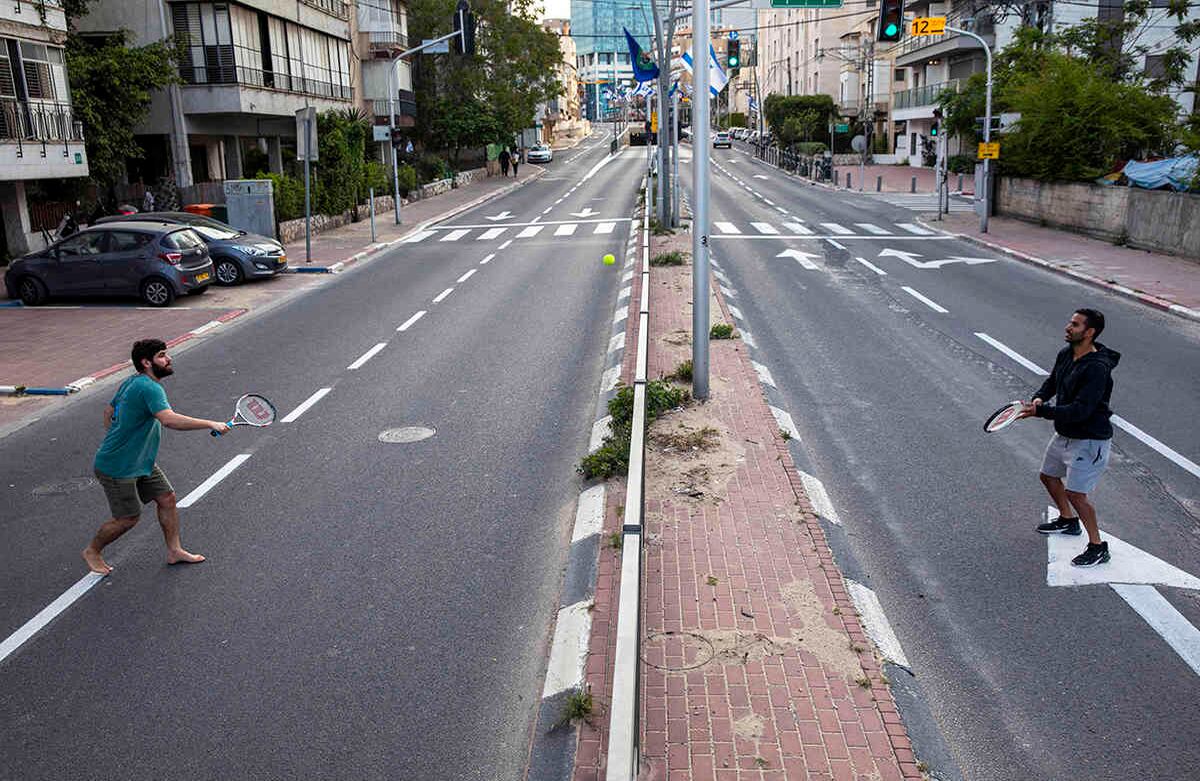 Israelíes juegan al tenis en una carretera vacía durante el aislamiento por las medidas del gobierno para ayudar a detener la propagación del coronavirus, en Ramat Gan, cerca de Tel Aviv, Israel, el jueves 9 de abril de 2020. AP Photo/Oded Balilty