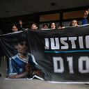 Los fanáticos de Diego Maradona gesticulan mientras sostienen una bandera con la imagen del fallecido, frente al tribunal de San Isidro. (Foto Luis ROBAYO / AFP)