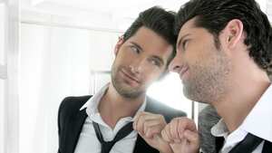 Guapo traje narcisista orgulloso joven mirándose en el espejo